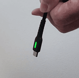 A hand holding the end of a charging cable with a green light on it