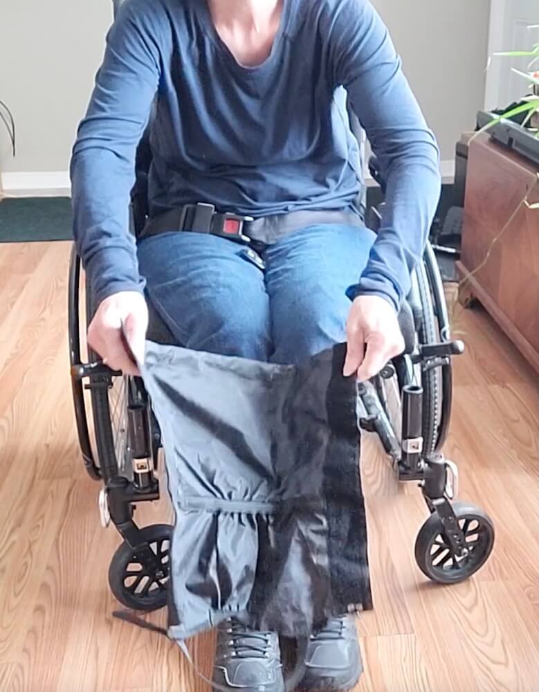 A person in a wheelchair has the gaiter open, with the buckle at the bottom connecting the sides.