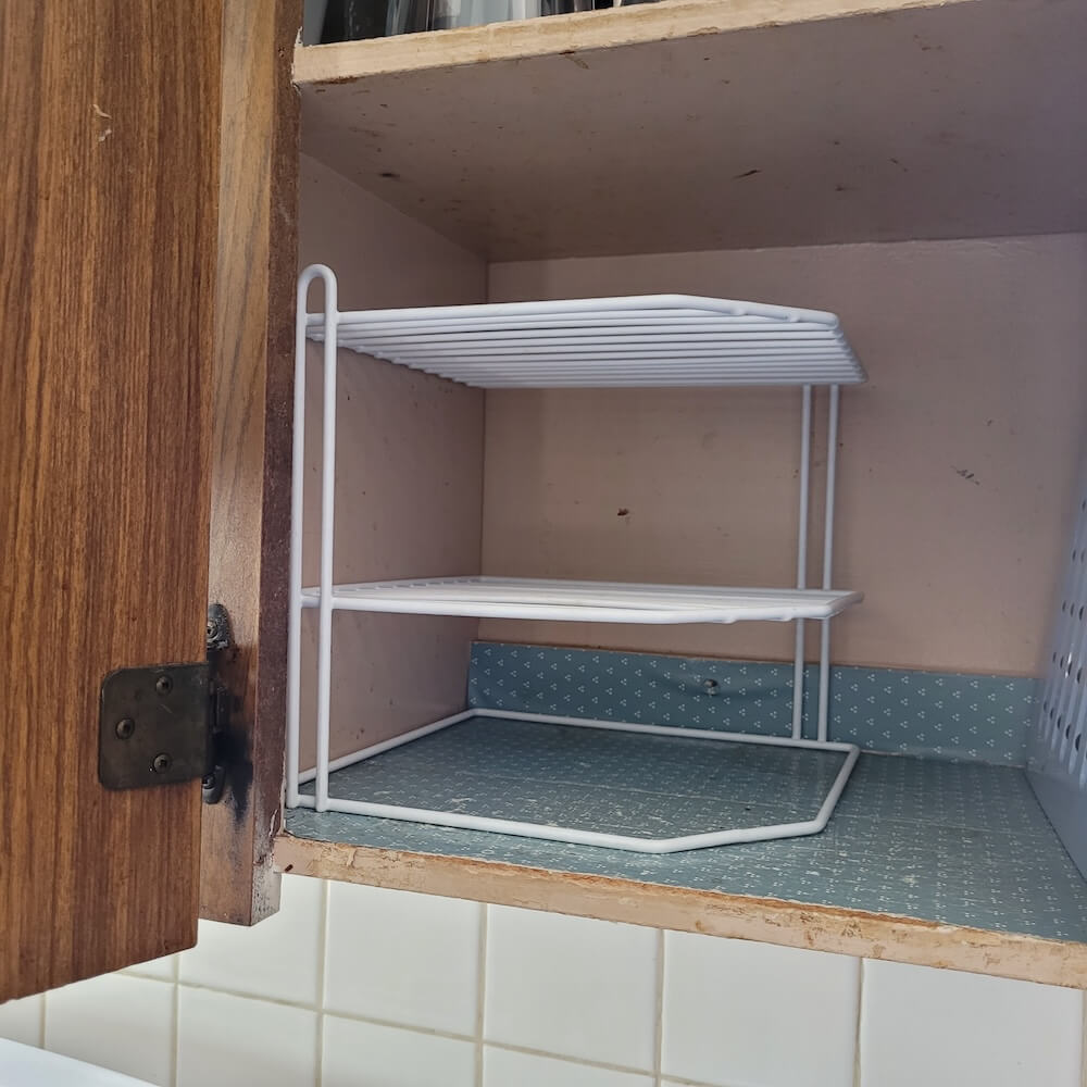 Corner rack sitting in shelf without any plates. The rack is white and creates two additional shelves in the cabinet.