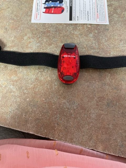 Safety light with velcro strap attached. The light is oval shaped and red, with a gray button at the bottom of it.